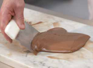 spreading chocolate out on a slab with a scraper